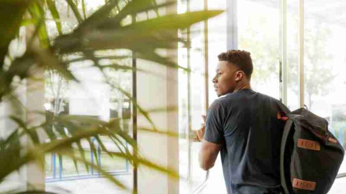 A college student with a backpack exits a campus building through glass doors., tags: die universität canterbury - pexel